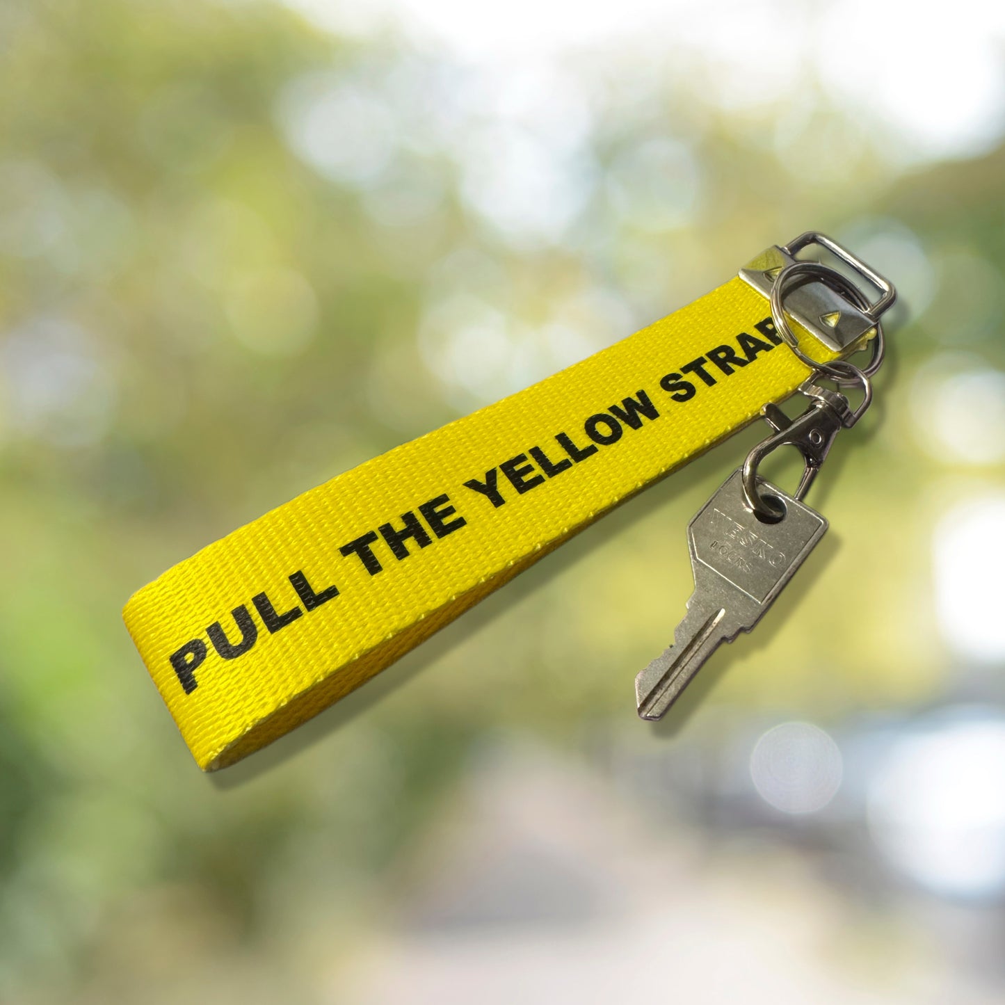 May include: A yellow security strap with a metal ring. The strap has black text that reads 'VOID IF TAMPERED' and 'DO NOT PAINT OVER OR REMOVE LABEL'. A barcode and other text are printed on the strap. The strap is angled against a background with a blur decorations.
