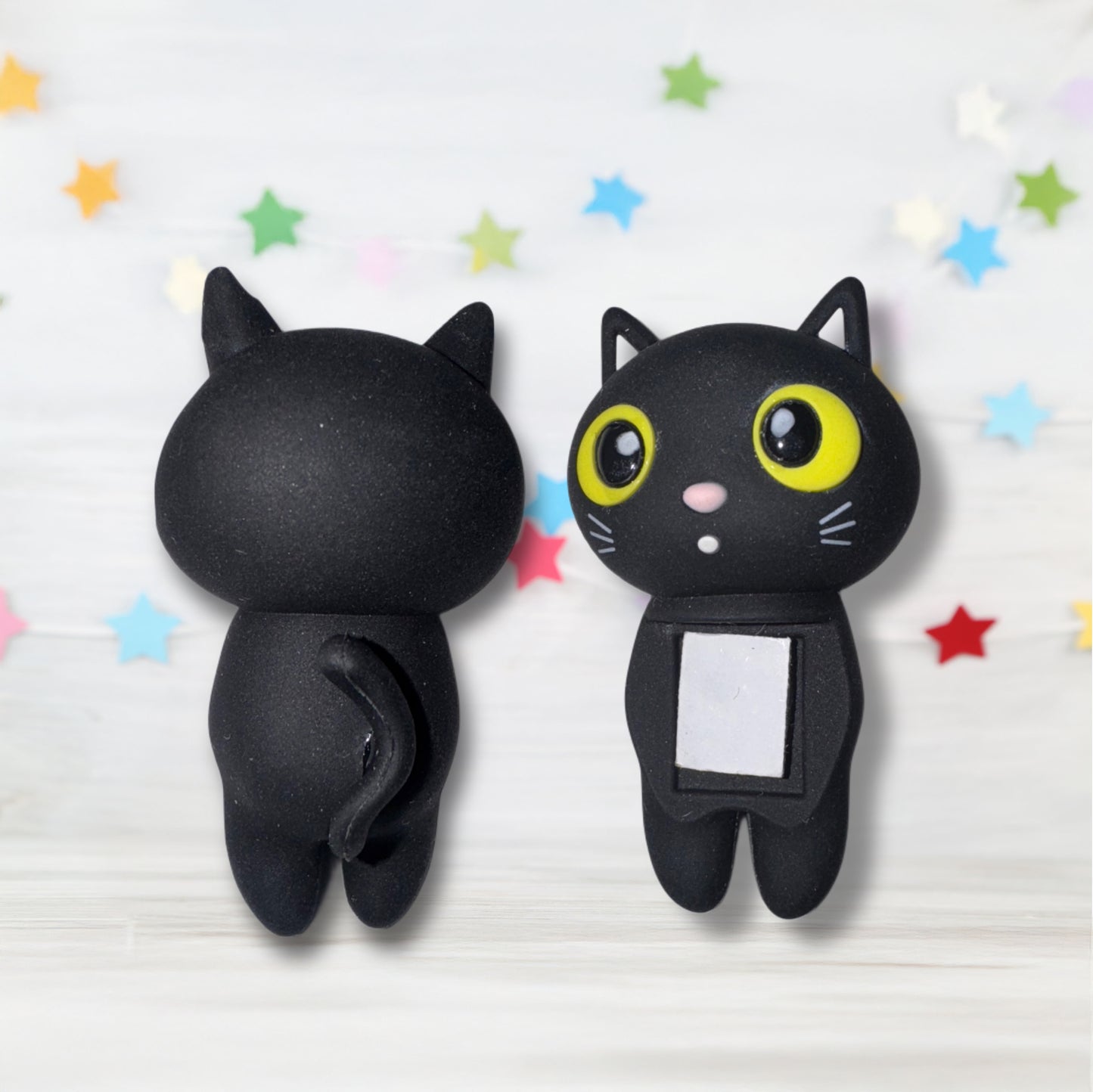 Two black cat-shaped clips with one having a small square attached on a light background with colorful stars.