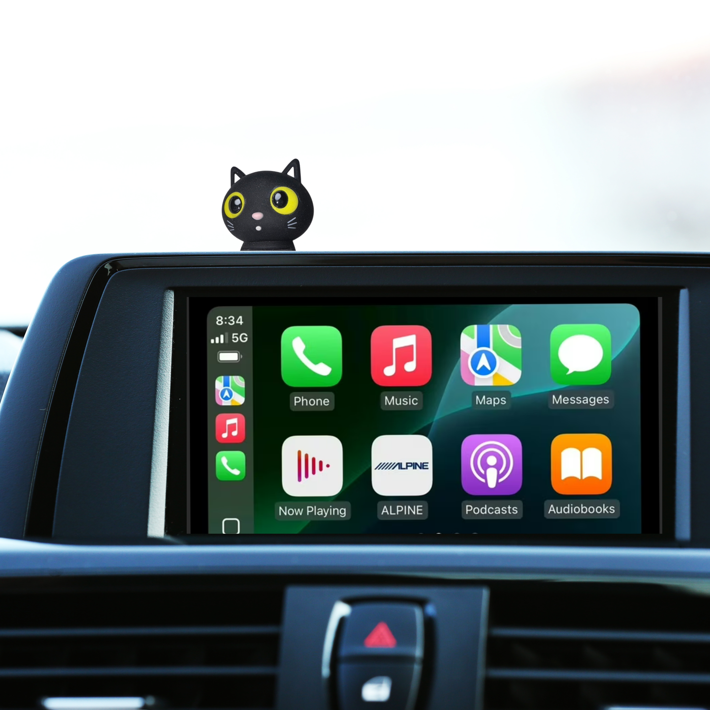 Car dashboard with a navigation screen displaying app icons and a a Black cat figurine with yellow eyes 