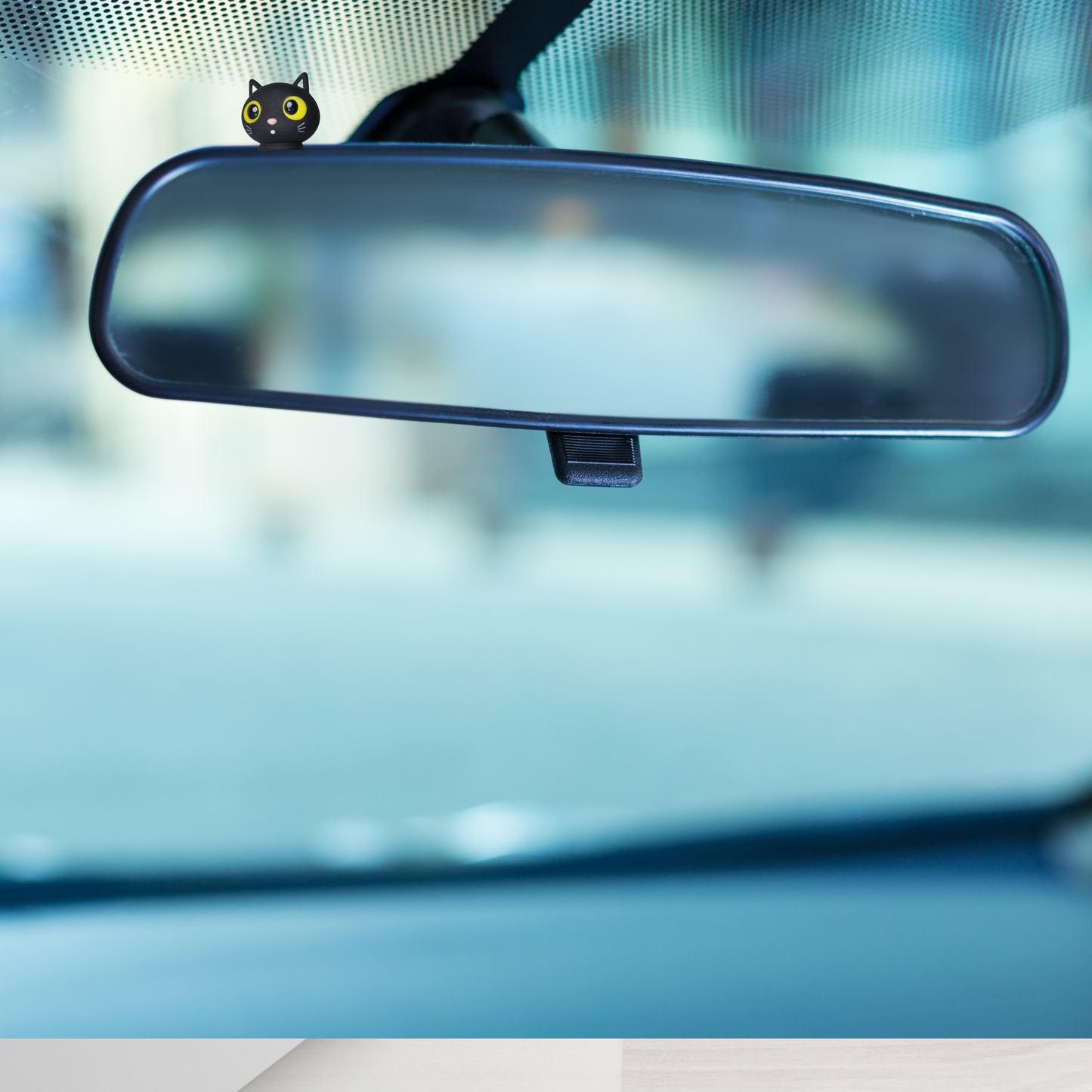 Car interior with a Black cat figurine with yellow eyes on a rearview mirror with blurred background  